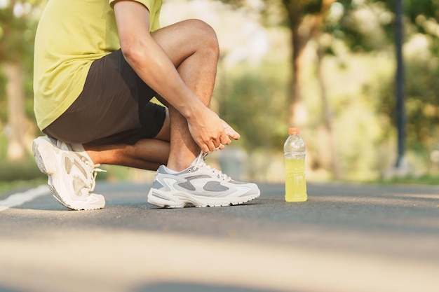 Młody sportowiec wiąże buty do biegania z wodą Energy Drink męski biegacz gotowy do joggingu poza azjatą Fitness spacery i ćwiczenia w parku rano dobre samopoczucie i koncepcje sportowe