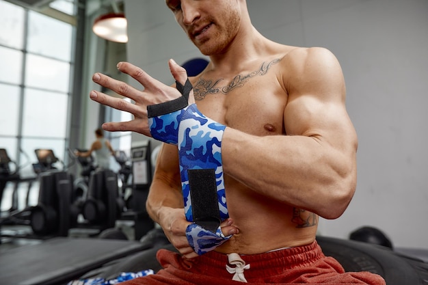 Młody sportowy przystojny mężczyzna owija ręce bandażem gimnastycznym, przygotowując się do ćwiczeń ze sztangą