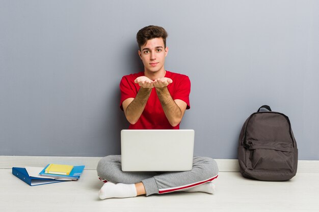 Młody studencki mężczyzna obsiadanie na jego domowej podłoga trzyma laptop