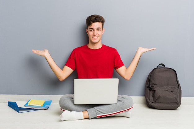 Młody studencki mężczyzna obsiadanie na jego domowej podłoga trzyma laptop