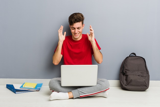 Młody studencki mężczyzna obsiadanie na jego domowej podłoga trzyma laptop