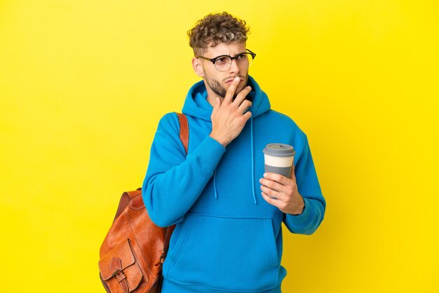 Młody student blond mężczyzna na żółtym tle ma wątpliwości podczas patrzenia w górę