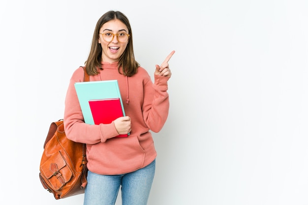 Młody student kaukaski kobieta na białym tle na białej ścianie uśmiechnięty radośnie, wskazując palcem wskazującym z dala.