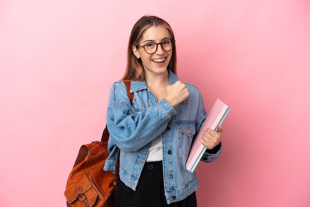 Młody student kaukaski kobieta na różowym tle świętuje zwycięstwo