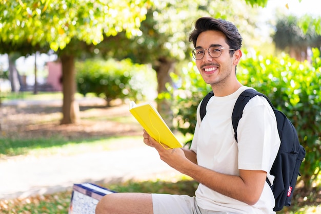 Młody student mężczyzna na zewnątrz, trzymając zeszyt