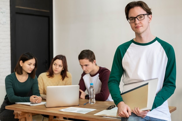 Młody student podczas grupowej nauki pozuje przy biurku