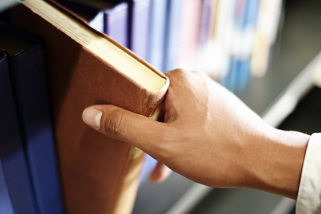 Młody student uczeń trzyma książkę pod ręką lub zrywanie książki na półce w tle regały biblioteczne - koncepcja edukacji biznesowej