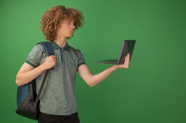 Młody student w dżinsach z plecakiem trzymający laptopa w dłoniach Izolowany na zielonym tle Studia na uniwersytecie online Komunikacja wideo Kwarantanna