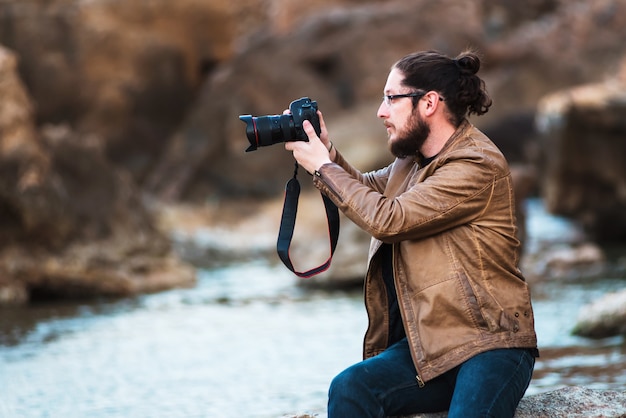 Młody Stylowy Fotograf Siedzi Na Skale Plaży I Robi Zdjęcie Morza