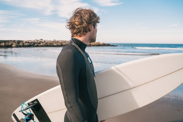 Młody surfer stojący w oceanie z deską surfingową w czarnym garniturze do surfingu