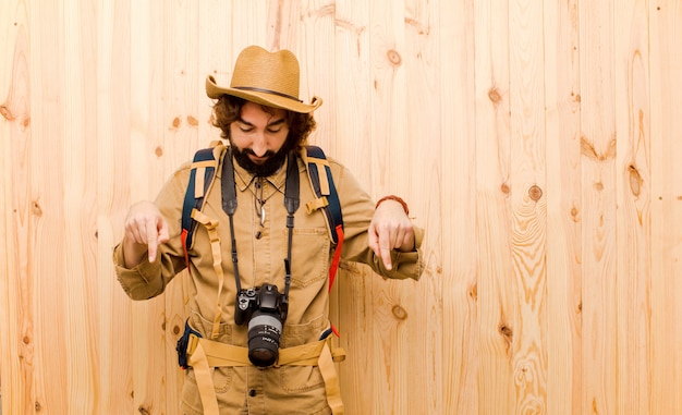 Młody szalony badacz z słomianym kapeluszem i plecakiem na drewnianej ścianie