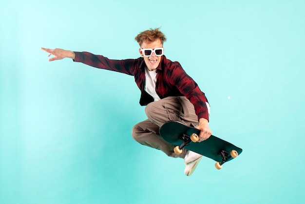 Młody szalony facet jeździ na deskorolce i skacze na niebieskim izolowanym tle hipster w okularach przeciwsłonecznych lata