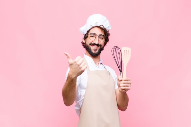 Młody szalony piekarz człowiek z narzędziem kucharz przed różową ścianą