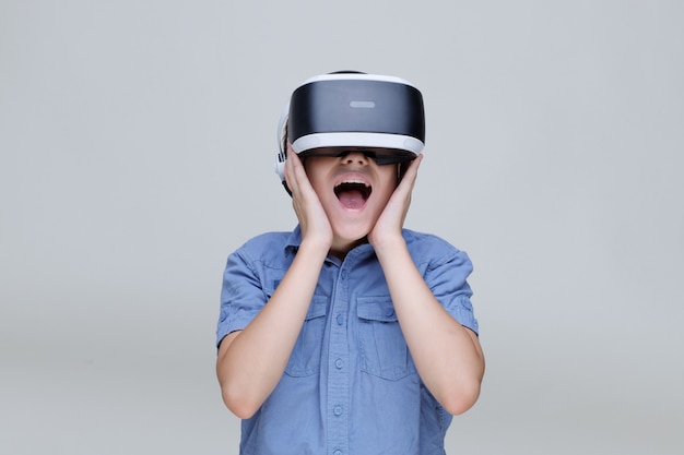 młody szczęśliwy chłopiec w okularach wirtualnej rzeczywistości na szarym tle