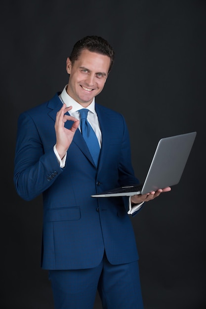 Młody szczęśliwy człowiek biznesu z ok gestem i laptopem