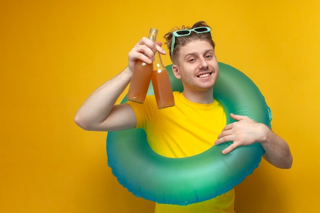 Młody szczęśliwy facet latem na wakacjach trzyma butelki piwa i uśmiecha się na żółtym tle
