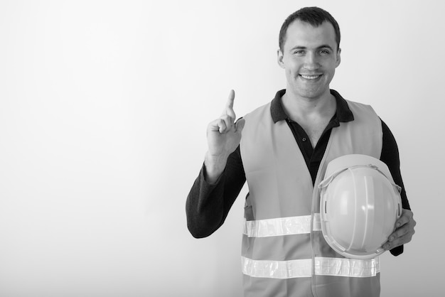 młody szczęśliwy muskularny mężczyzna robotnik budowlany uśmiecha się trzymając kask i skierowaną w górę