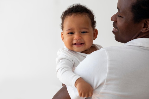 Młody szczęśliwy ojciec trzymający urocze, uśmiechnięte małe czarne dziecko w ramionach