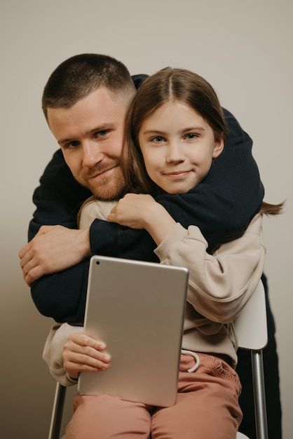 Młody szczęśliwy ojciec z brodą przytula swoją śliczną córkę za pomocą tabletu