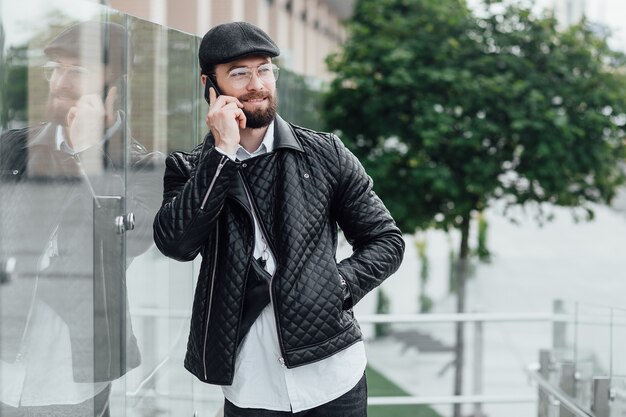 Młody, szczęśliwy, przystojny, stylowy mężczyzna rozmawia przez telefon komórkowy na ulicach miasta