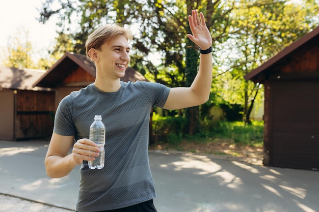Młody szczęśliwy wysportowany mężczyzna pije wodę po treningu