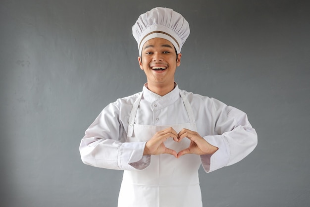 Młody szef kuchni w białym toczku i fartuchu uśmiecha się i robi rękami kształt symbolu serca.