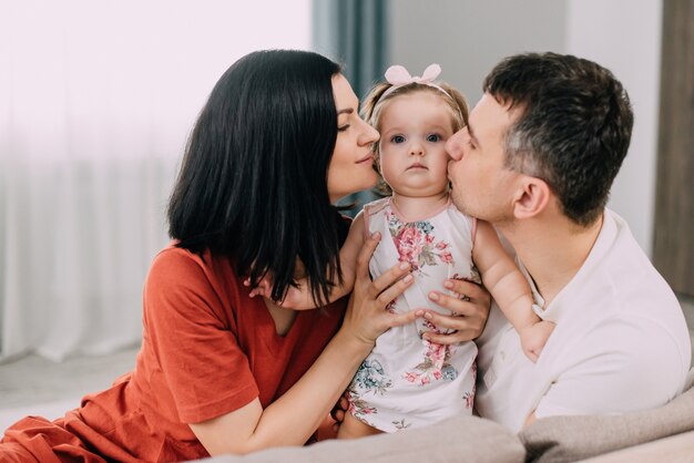 Młody Tata I Mama Przytulają Swoją Roczną Córkę, Siedząc Na Kanapie W Domu.