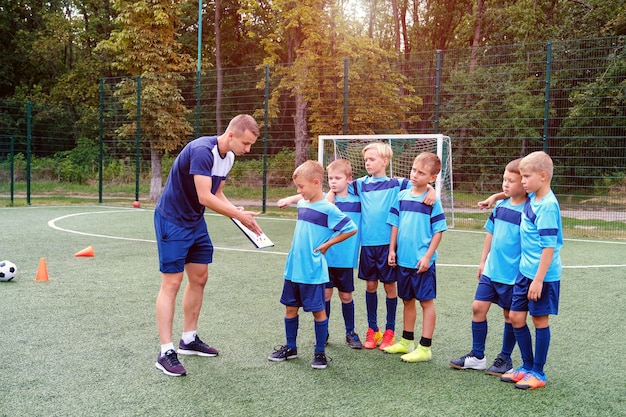 Młody trener uczy małe dzieci strategii gry na boisku piłkarskim