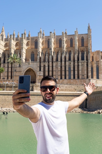 Młody turysta mężczyzna fotografujący się przed katedrą w Palma de Mallorca w słoneczny dzień w Hiszpanii