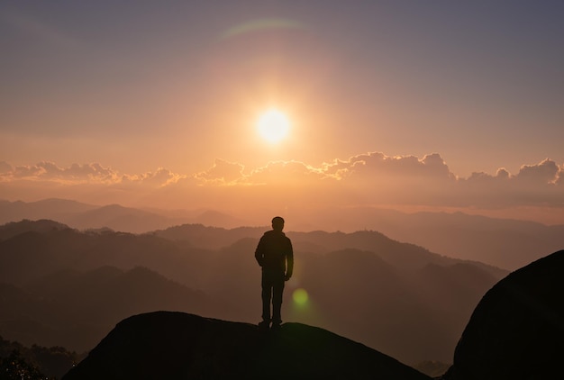 Młody turysta mężczyzna stojący na szczycie góry ze słońcem o zachodzie słońca