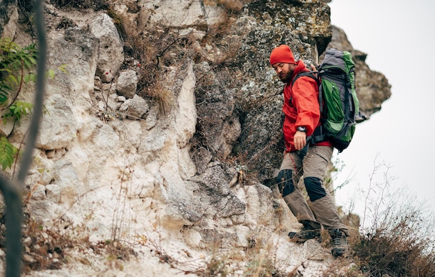 Młody turysta mężczyzna wędrówki w górach ubrany w czerwone ubrania odkrywanie nowego miejsca Brodaty mężczyzna podróżujący trekking i wspinaczka górska podczas podróży Podróż ludzie sport i zdrowy styl życia koncepcja