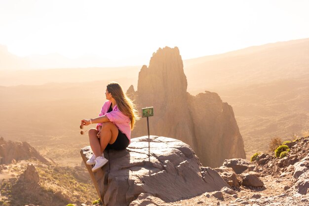 Młody turysta siedzący w różowej bluzie i patrzący na zachód słońca na naturalnym obszarze Teide na Wyspach Kanaryjskich Teneryfa