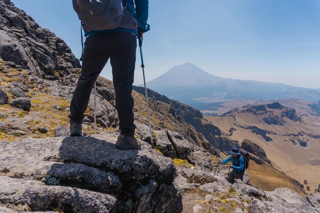 Młody turysta z plecakiem i kijkami trekkingowymi stojący na krawędzi klifu i patrzący na góry