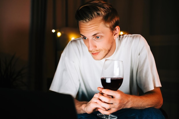 Zdjęcie młody tysiącletni mężczyzna prowadzi rozmowę wideo na laptopie i pije wino