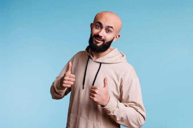 Młody uśmiechnięty arabski mężczyzna wyrażający akceptację z aprobatami i pozytywnymi emocjami. Wesoła osoba ubrana w zwykłe ubrania, wykazująca aprobatę podobnym znakiem i patrząca w kamerę