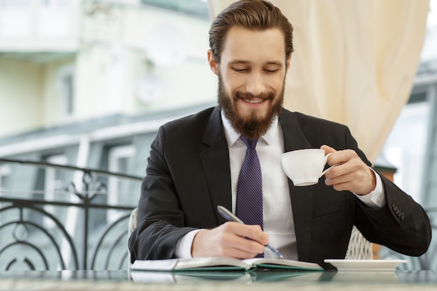 Młody uśmiechnięty biznesmen bierze notatki podczas jego śniadania przy restauracją