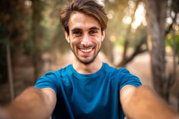 Zdjęcie młody uśmiechnięty kaukazyjski mężczyzna robi selfie w lesie patrząc na kamerę