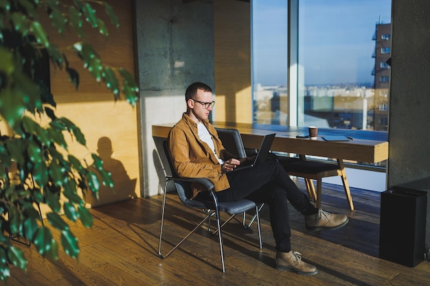 Młody uśmiechnięty mężczyzna freelancer pracujący zdalnie w przestronnym nowoczesnym biurze Menedżer w wygodnych ubraniach pracuje zrelaksowany w biurze