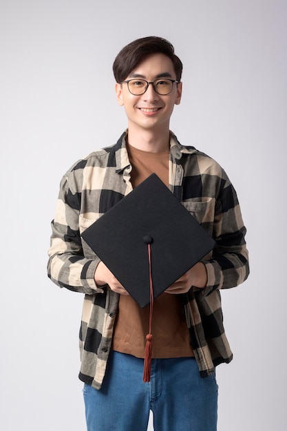 Młody uśmiechnięty mężczyzna trzyma ukończenie studiów kapelusz edukacja i uniwersytecka koncepcjax9