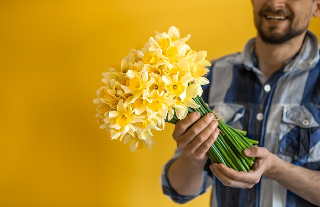 Młody uśmiechnięty mężczyzna z bukietem wiosennych kwiatów na kolorowej ścianie