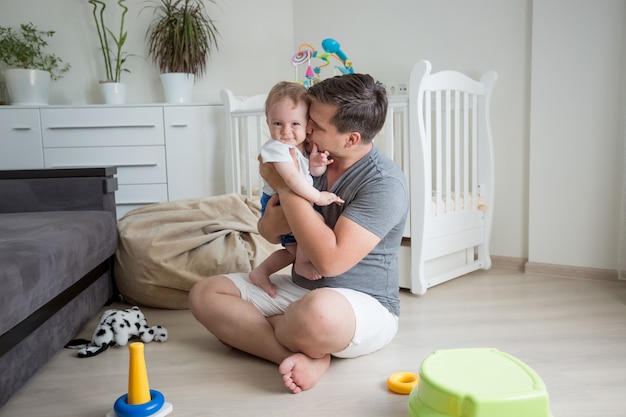 Młody uśmiechnięty ojciec bawi się ze swoją podłogą na podłodze w sypialni