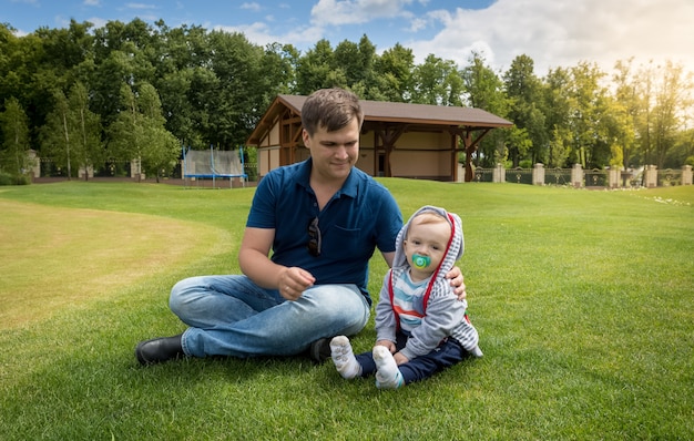 Młody uśmiechnięty ojciec z synkiem relaksuje się na trawie w parku w słoneczny dzień