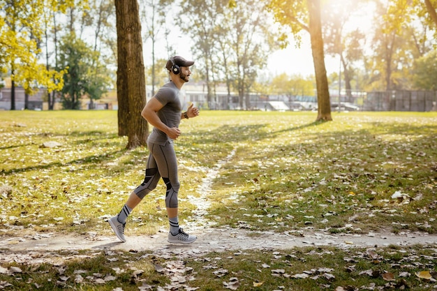 Młody uśmiechnięty sportowiec ze słuchawkami jogging w przyrodzie.