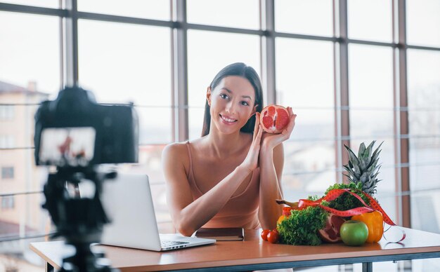 Młody vloger fitness robi wideo w pomieszczeniu, siedząc przy stole ze zdrową żywnością.