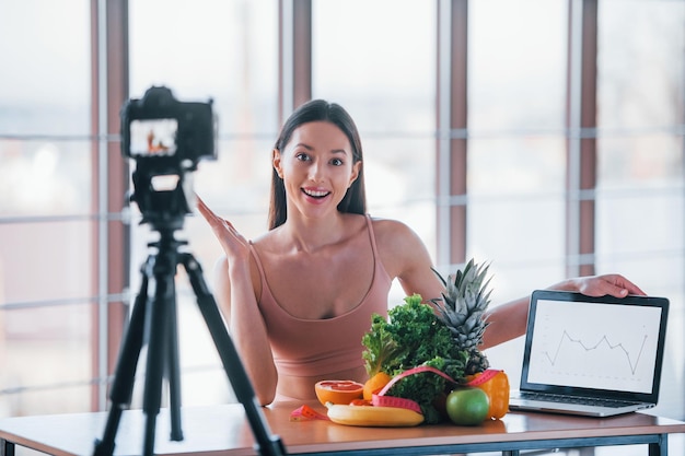 Młody vloger fitness robi wideo w pomieszczeniu, siedząc przy stole ze zdrową żywnością.