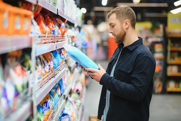 Młody wesoły pozytywny męski klient robi zakupy w supermarkecie kupując chemię gospodarczą