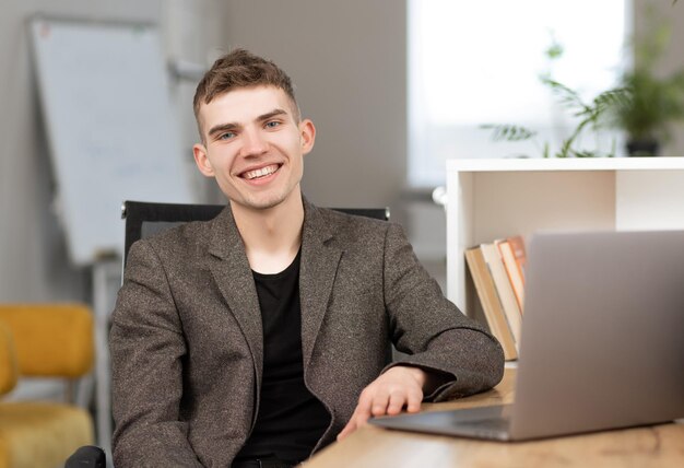 Młody wesoły programista pracujący w biurze na laptopie