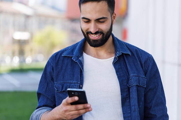 Młody, wielokulturowy mężczyzna trzyma w swoim telefonie komórkowym przewijanie wiadomości tekstowych