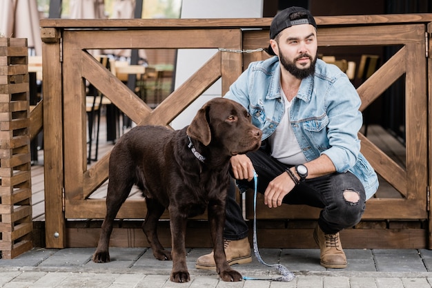 Młody Właściciel Rasowego Brązowego Labradora Kucającego Przy Drewnianych Furtkach Podczas Relaksu Ze Swoim Słodkim Zwierzakiem