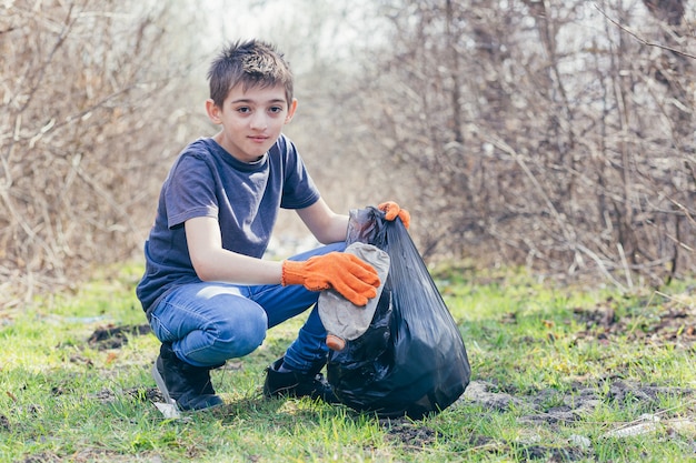 Młody Wolontariusz Zbiera śmieci W Lesie Ubrany W Pomarańczowe Rękawiczki Wkłada Plastikowe Butelki Do Worka Na śmieci